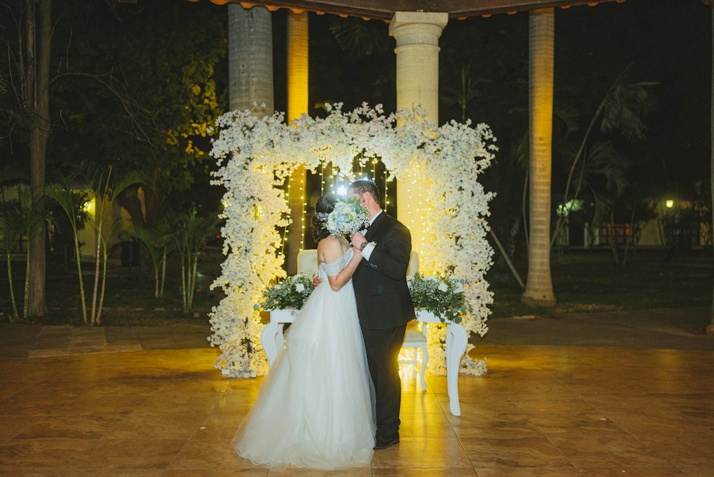 A couple embracing under a floral arch lit with warm lights